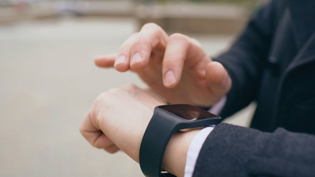Image of a person charging their smartwatch via wireless charger, desk setup visible.