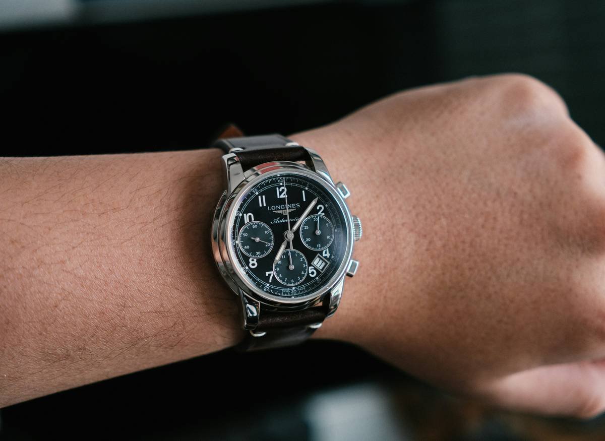Side-by-side comparison of a bulky fitness tracker vs. a slim hybrid smartwatch on a tailored shirt cuff